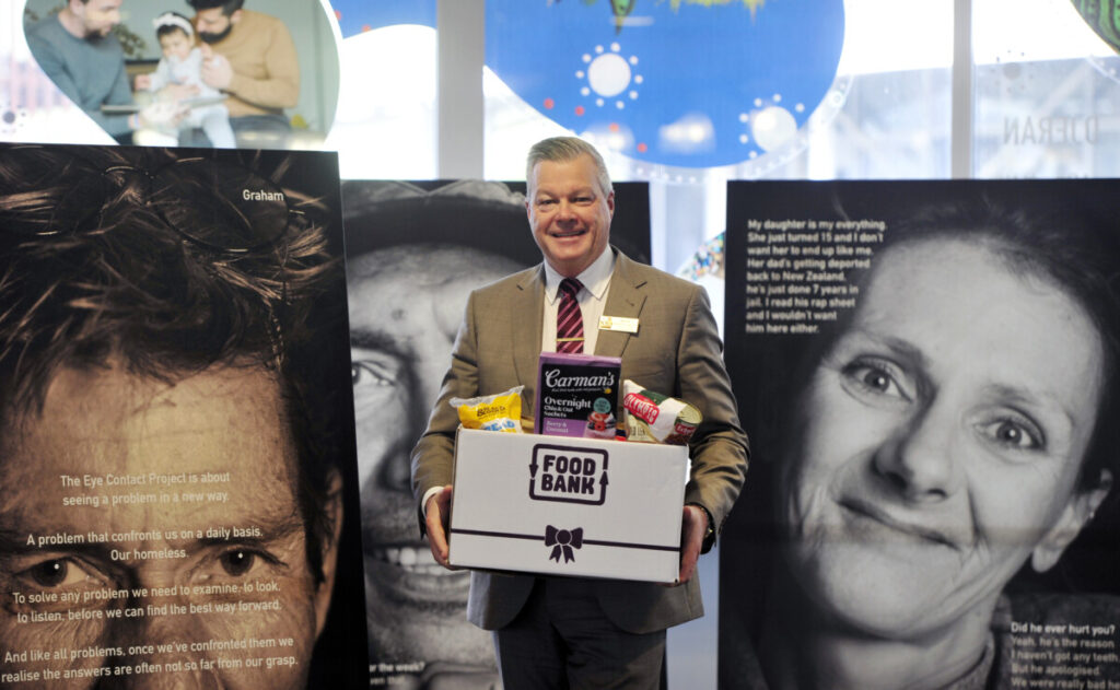 Mayor in front of homelessness photos holding food.