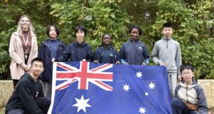 A teacher and seven students pose for photo holding Australian flag.