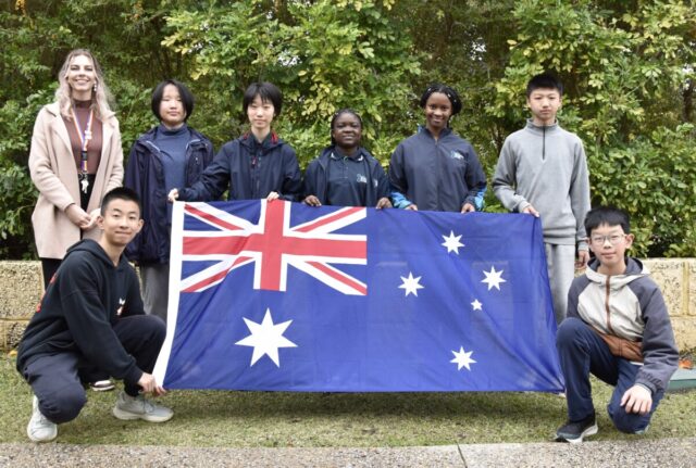 A teacher and seven students pose for photo holding Australian flag.