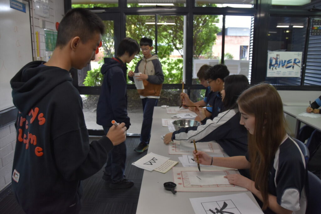 Students in a class room holding drawing brushes. 