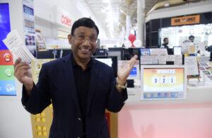 Man puts hands in air, shrugging his shoulders, while holding lotto ticket.