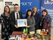 People holding with award frame in front of food donations.