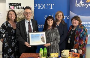 People holding with award frame in front of food donations.