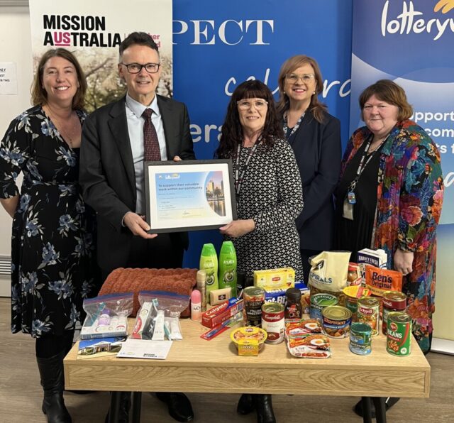 People holding with award frame in front of food donations.