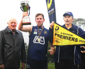 Three men with the two on the right holding a premiership flag and trophy.